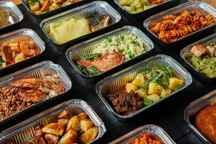 Foil trays of various lunch items including salmon, pasta, chicken, steak