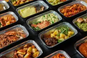 Foil trays of various lunch items including salmon, pasta, chicken, steak
