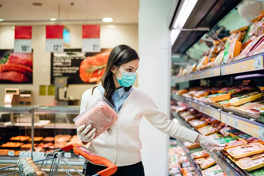 Women shopping in a grocery store meat aisle during COVID